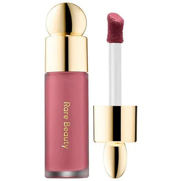 Liquid blush applicator dispensing a drop of product onto a makeup brush with a soft background.