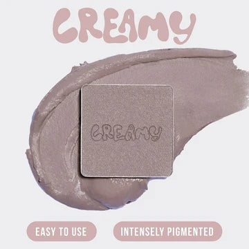 Top-down flatlay of Huda Beauty Creamy Obsessions Greige palette open with all 9 cream-to-powder eyeshadows displayed: grey-brown cream, grey marble, light pink, pinky-grey, grey metallic, blue-grey, purple-grey metallic, neutral pink matte, and black-grey cream