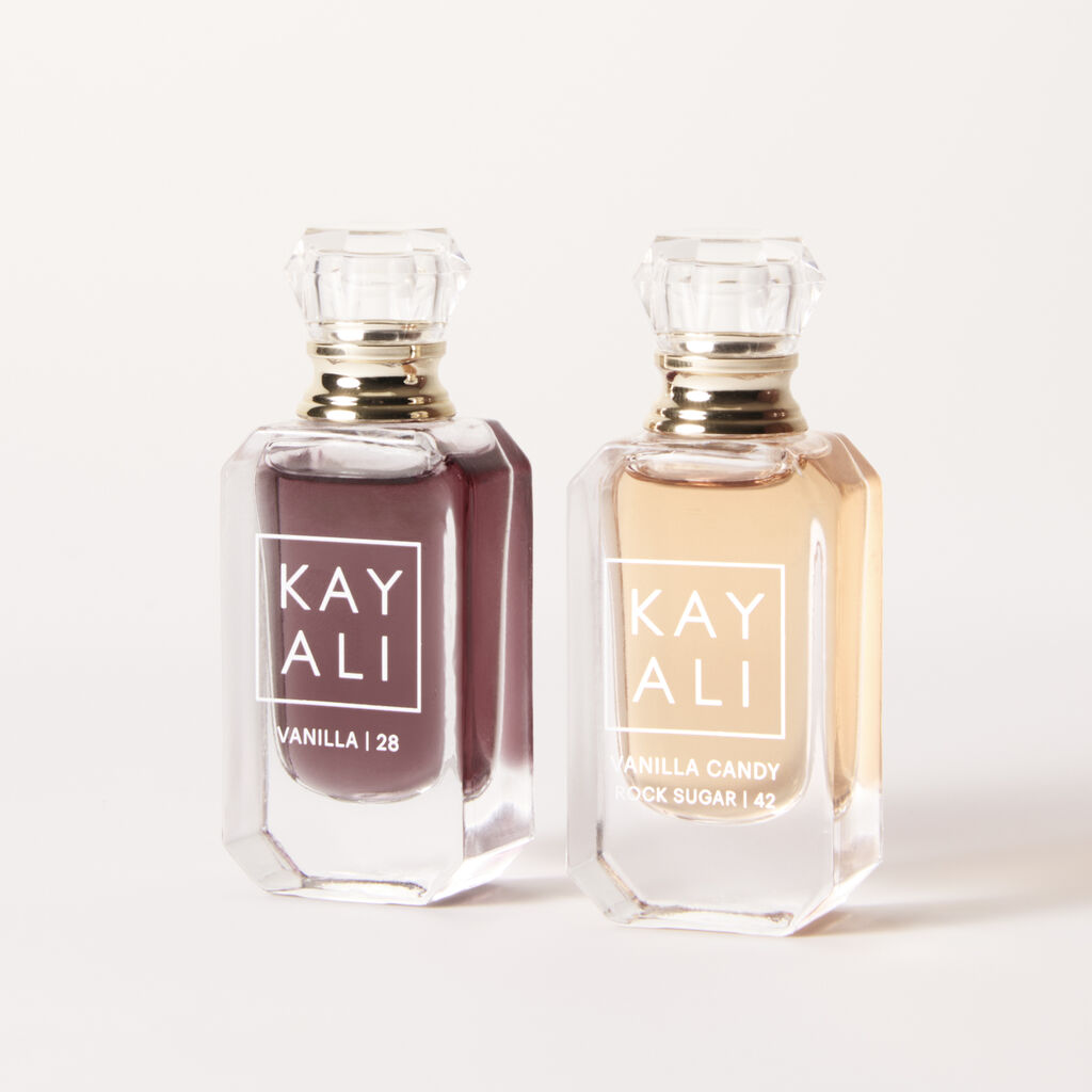 HUDA BEAUTY Kayali Mini Vanilla Perfume Duo Set featuring two small bottles of vanilla perfume with gold caps. The text 'VANILLA 28' and 'VANILLA 128' is visible on the bottles, along with 'KAYALI' branding. Fragrance notes or descriptions may include 'STOXYEZ LOUIS BARBIN' and 'SCONNECTUM Z EMAY DE PARFUM