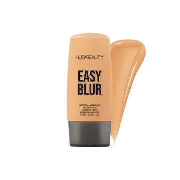 Close-up of Huda Beauty Mini Easy Blur Natural Airbrush Foundation in shade Creme Brulee, showing the 10ml travel-size tube with gold accents and product name visible.