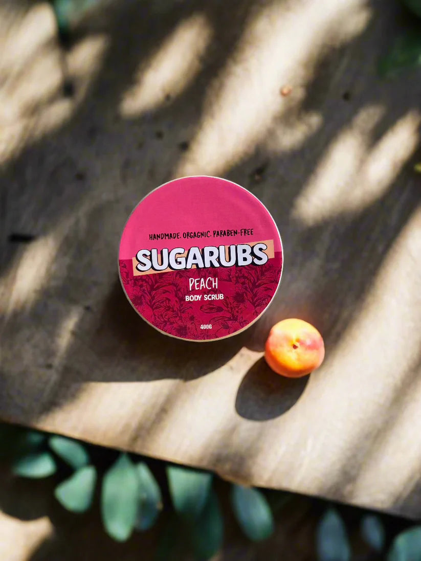 A jar of Peach Scrub placed beside fresh peaches and aloe vera leaves, showcasing its fresh and natural ingredients.