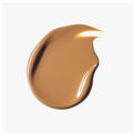 Bottle of tinted moisturizer on a soft beige background with shadows to highlight the dewy finish.

