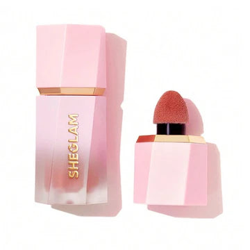 Close-up of Sheglam Color Bloom Dayglow Liquid Blush packaging in shade 'Devoted,' featuring a sleek tube with bold typography reading 'GET BOLD WITH OG MATTE SHADES!' The minimalist design includes silver accents and a doe-foot applicator for precise application