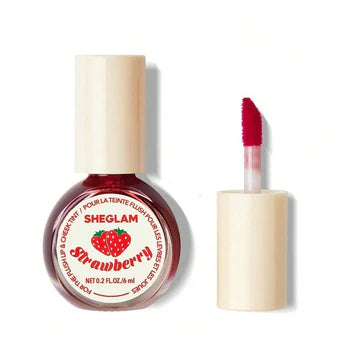 bottle of SHEGLAM For The Flush Lip & Cheek Tint in "Strawberry" is shown next to its cap with an applicator wand extended, displaying a vibrant red tint. The bottle's label includes "SHEGLAM" and "Strawberry" with a graphic of two strawberries