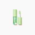 Close-up of SHEGLAM's hydrating lip oil in 'Green Apple Envy,' a glossy green formula designed to moisturize lips. The text 'BIGIRY WARM LIGHTWORK' hints at its lightweight, high-shine finish, housed in a sleek transparent tube