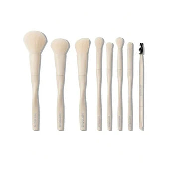 Flat lay demonstration of all 8 SHEGLAM Pro Core makeup brushes arranged in a circle, showcasing each brush type with labels: (1) Powder Brush – domed fluffy head, (2) Foundation Brush – dense flat shape, (3) Blush Brush – angled contour, (4) Eyeshadow Brush – tapered blending, (5) Small Shader Brush – compact oval, (6) Flame Brush – pointed tip, (7) Concealer Brush – short dense bristles, and (8) Eyebrow & Mascara Brush – dual-ended with spoolie. All feature matching beige handles and synthetic bristles