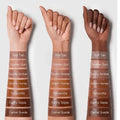Swatches of SHEGLAM Sun Sculpt Liquid Contour in seven shades (Soft Tan, Golden Sun, Ravity Amber, Warm Honey, Tetraextra, Equity Sepia, Camel Suede) displayed in rows on a neutral background. Each shade shows a warm-toned, highly pigmented liquid contour formula, ranging from light tan to deep amber, suitable for various skin tones
