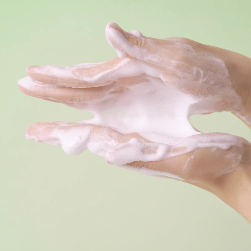 Hands with soap suds on a light green background