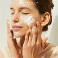 Person applying a skincare product to their face with 'SKIN1004' branding.