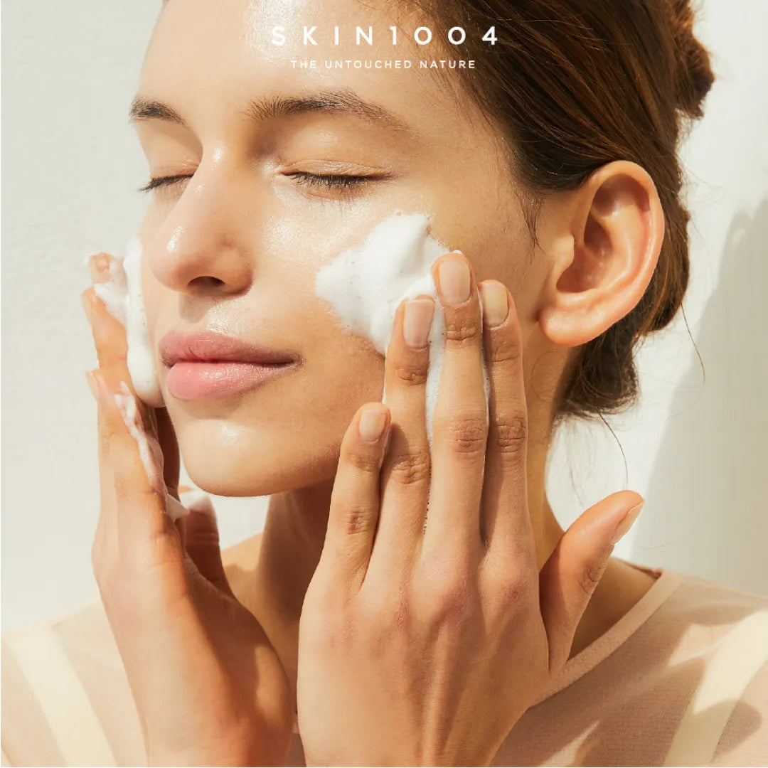 Person applying a skincare product to their face with 'SKIN1004' branding.