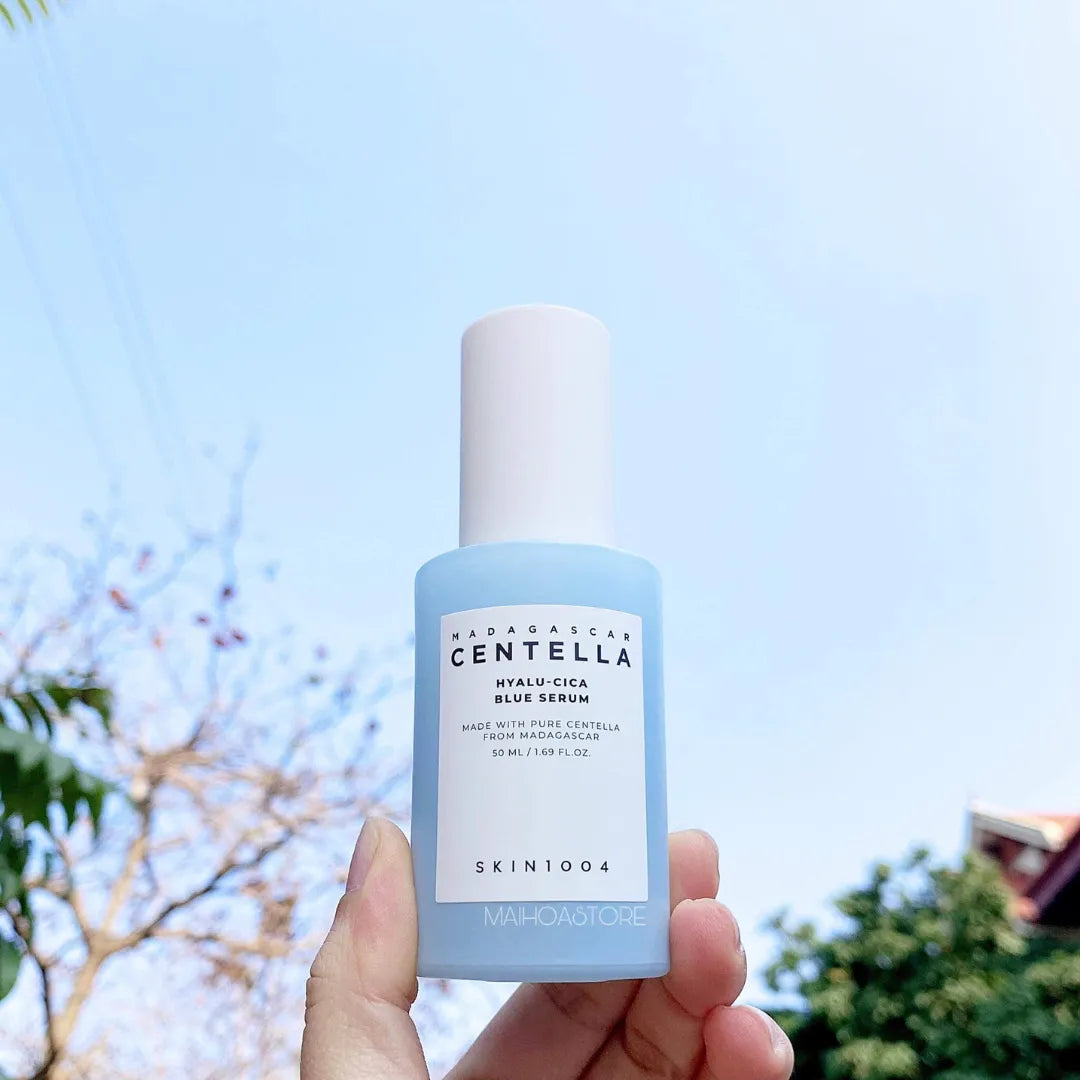 Hand holding a bottle of Skintouch Centella Hyalu-Cica Blue Serum against a blue sky background.