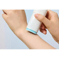 Hand using a white and blue roller on an arm against a light blue background