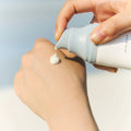 Hand applying skincare product from a 'SKIN1004' bottle to another hand against a light background