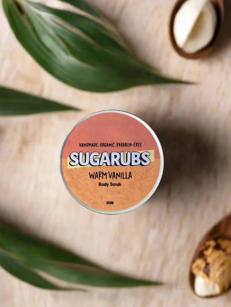 A jar of Warm Vanilla Body Scrub surrounded by vanilla beans and coconut slices, highlighting its natural ingredients.